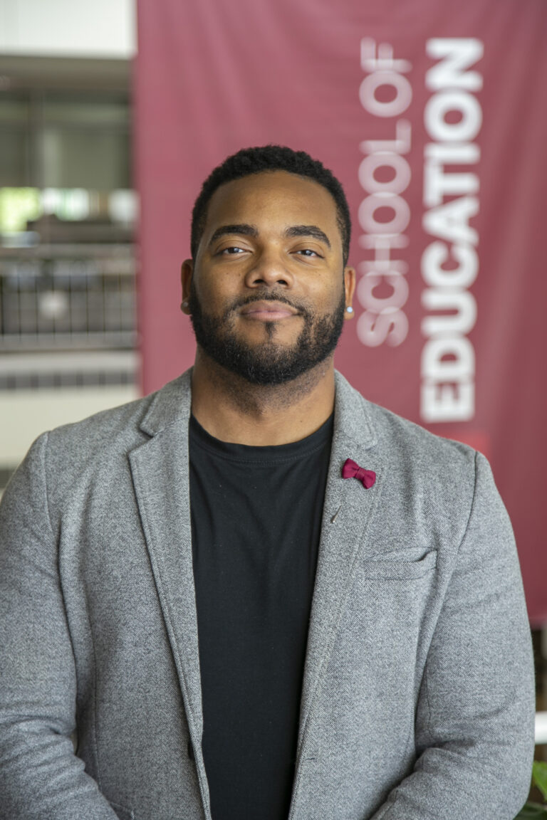 Dr. Leonard Taylor posing in front of a school of education flag